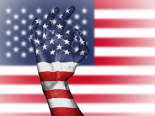 アメリカの国旗を背にOKマークを表示したイメージの写真